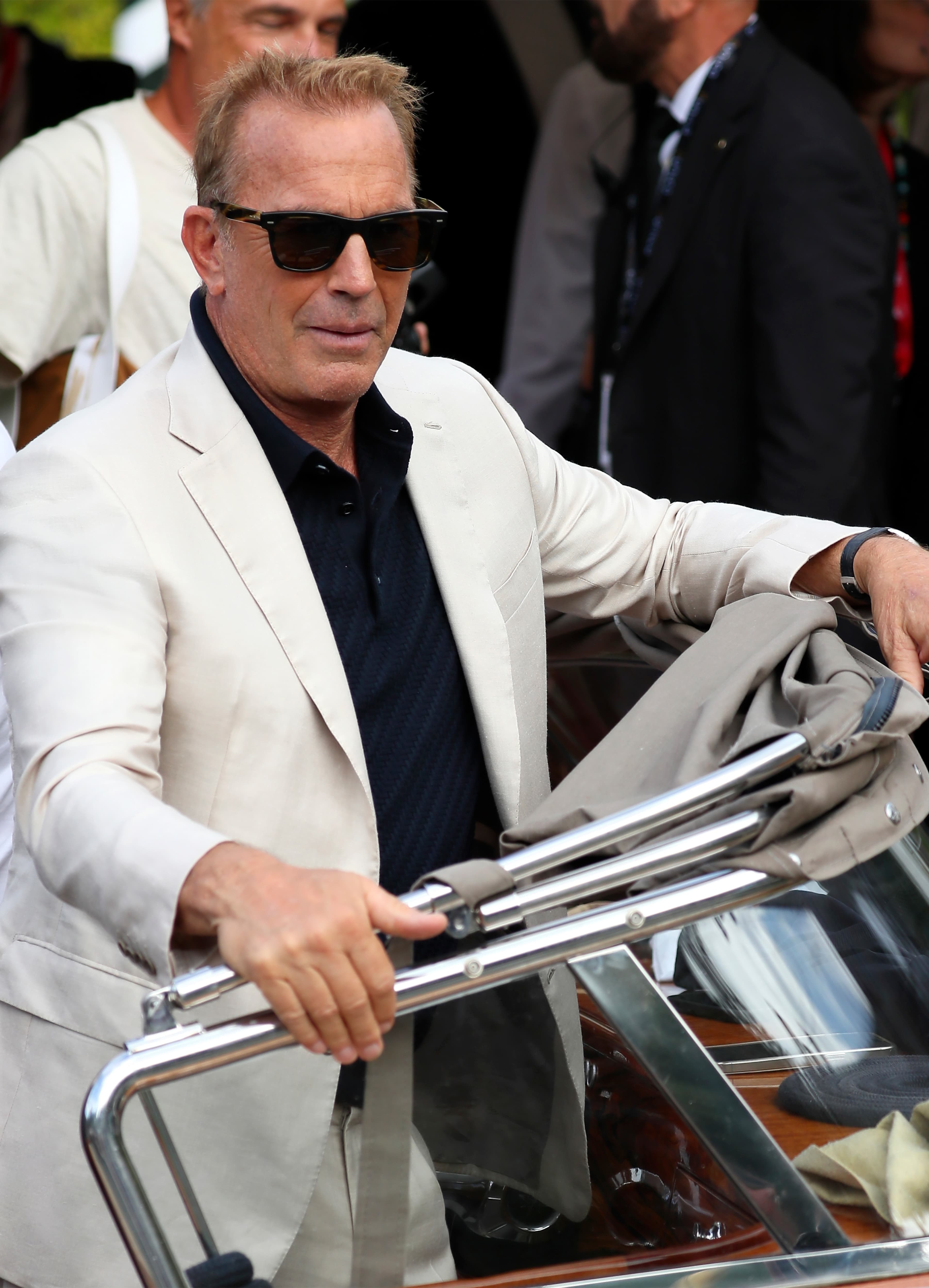 Kevin Costner in Brioni white blazer and sunglasses boarding a boat.