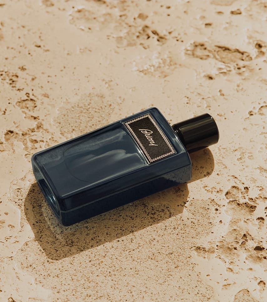 Eau de Parfum dark blue bottle with black cap resting on textured beige stone or marble surface.