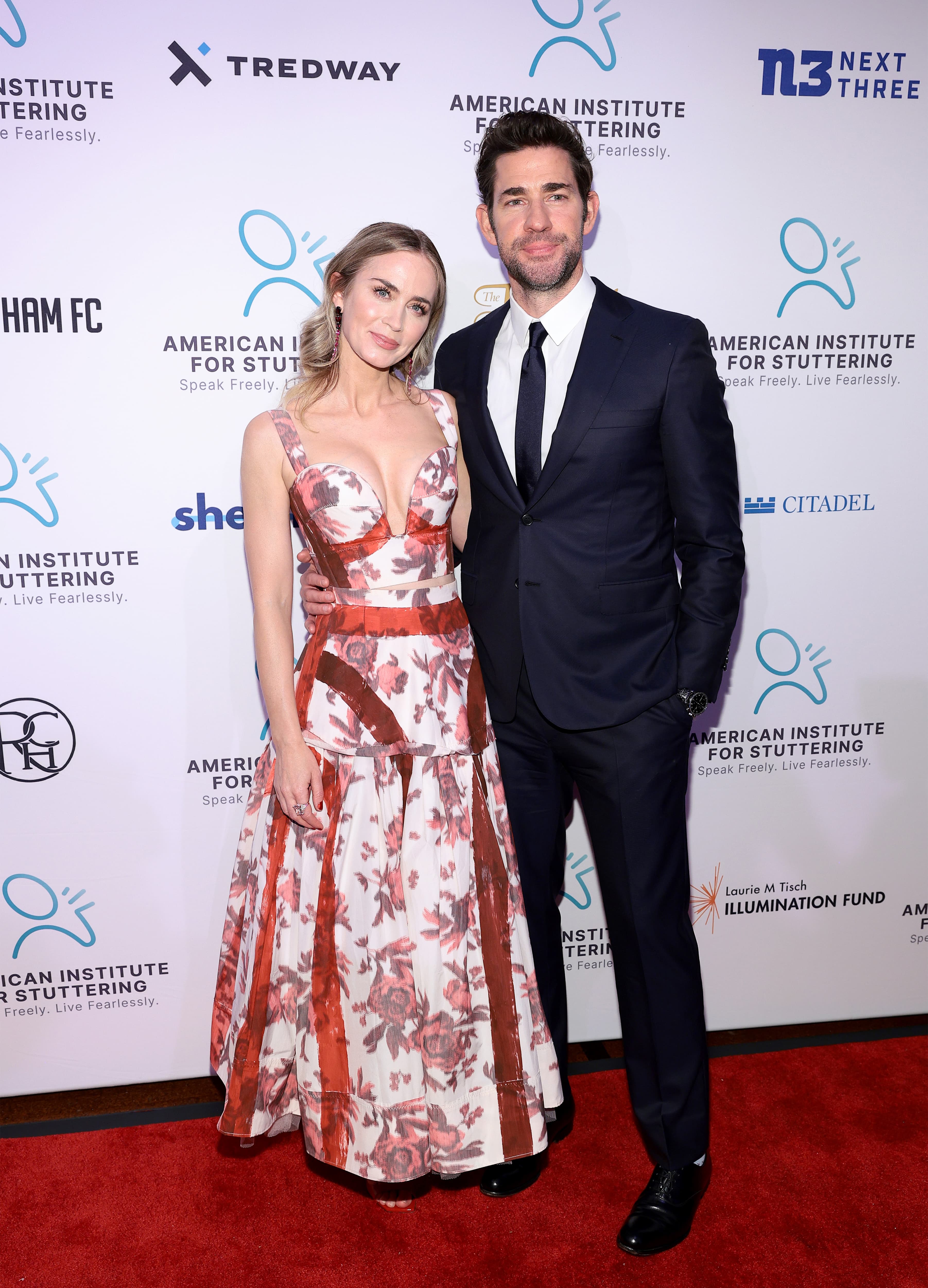 John Krasinski in a Brioni navy suit, standing on red carpet.