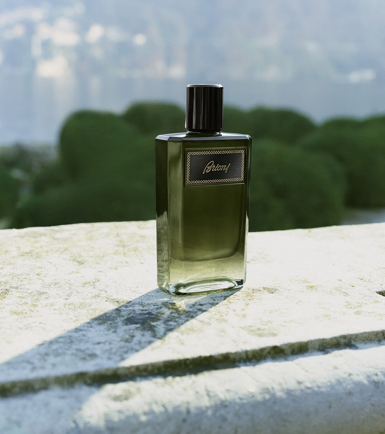 Elegant Essentiel green bottle on stone surface with blurred greenery and blue sky in background.