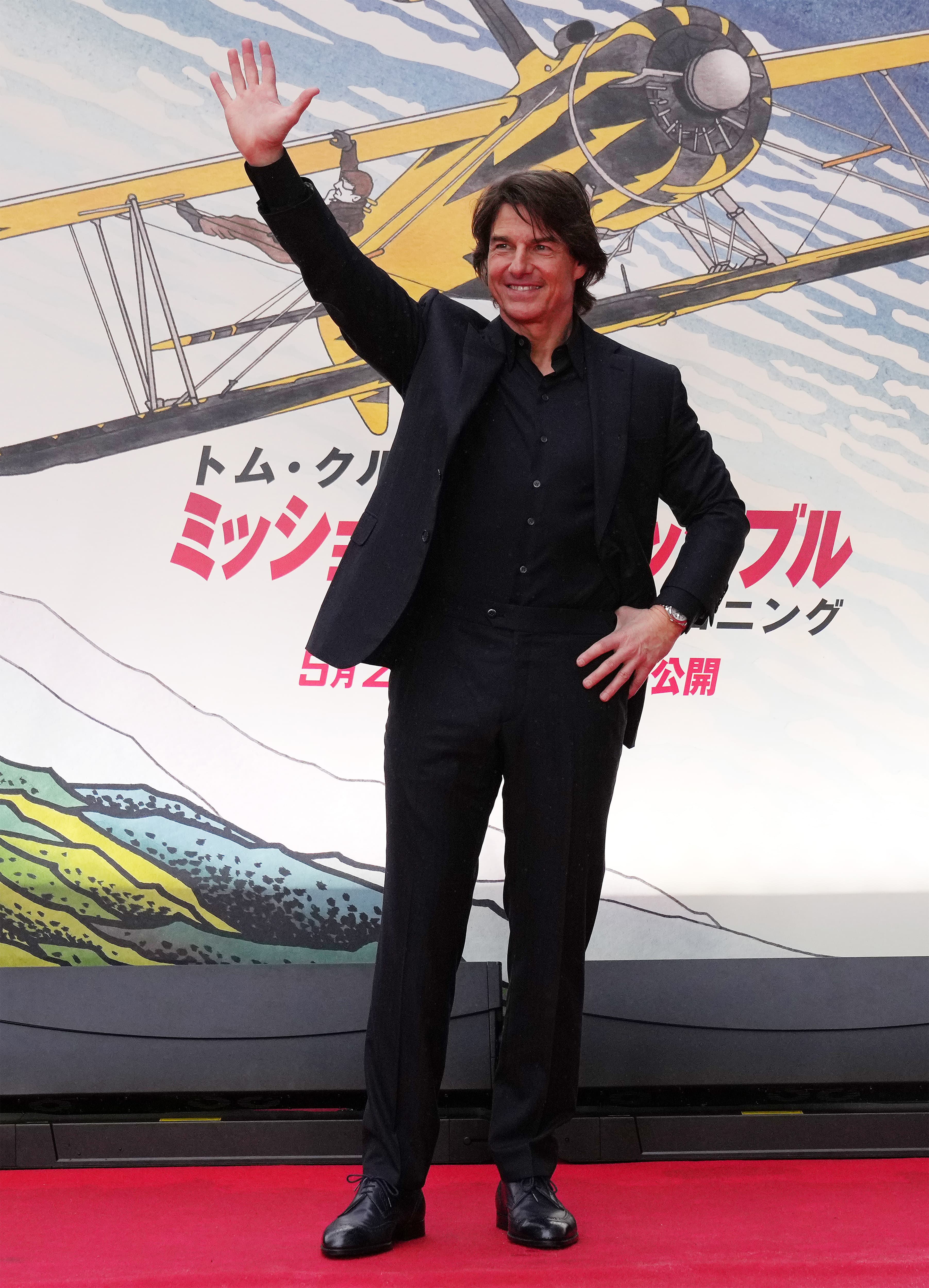 Tom Cruise in a Brioni black suit on red carpet with vintage yellow biplane promotional backdrop.