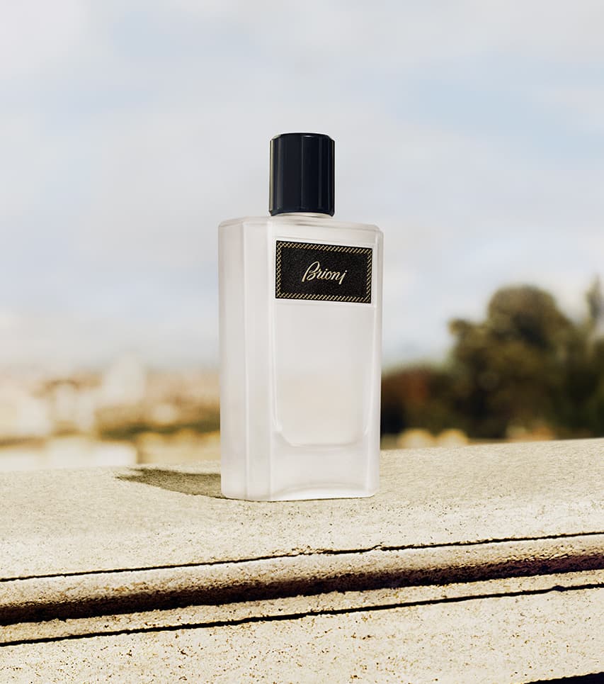 Elegant Eclat white bottle with black cap and gold label displayed on stone ledge against blurred outdoor background.