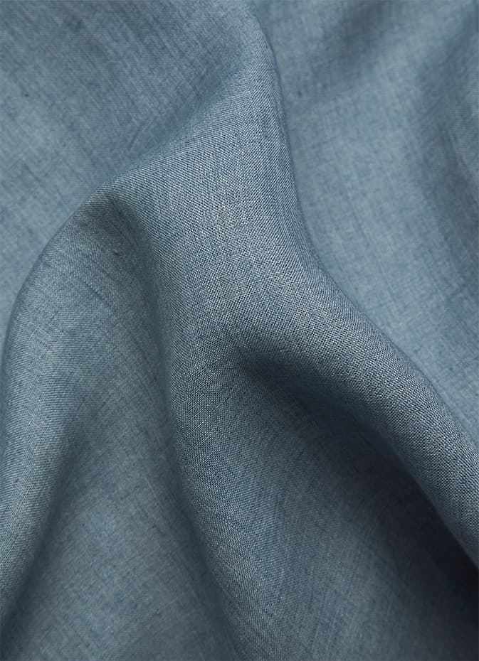 Close-up of Brioni soft blue-gray linen fabric with gentle folds and draping, showing detailed weave texture and natural wrinkles.
